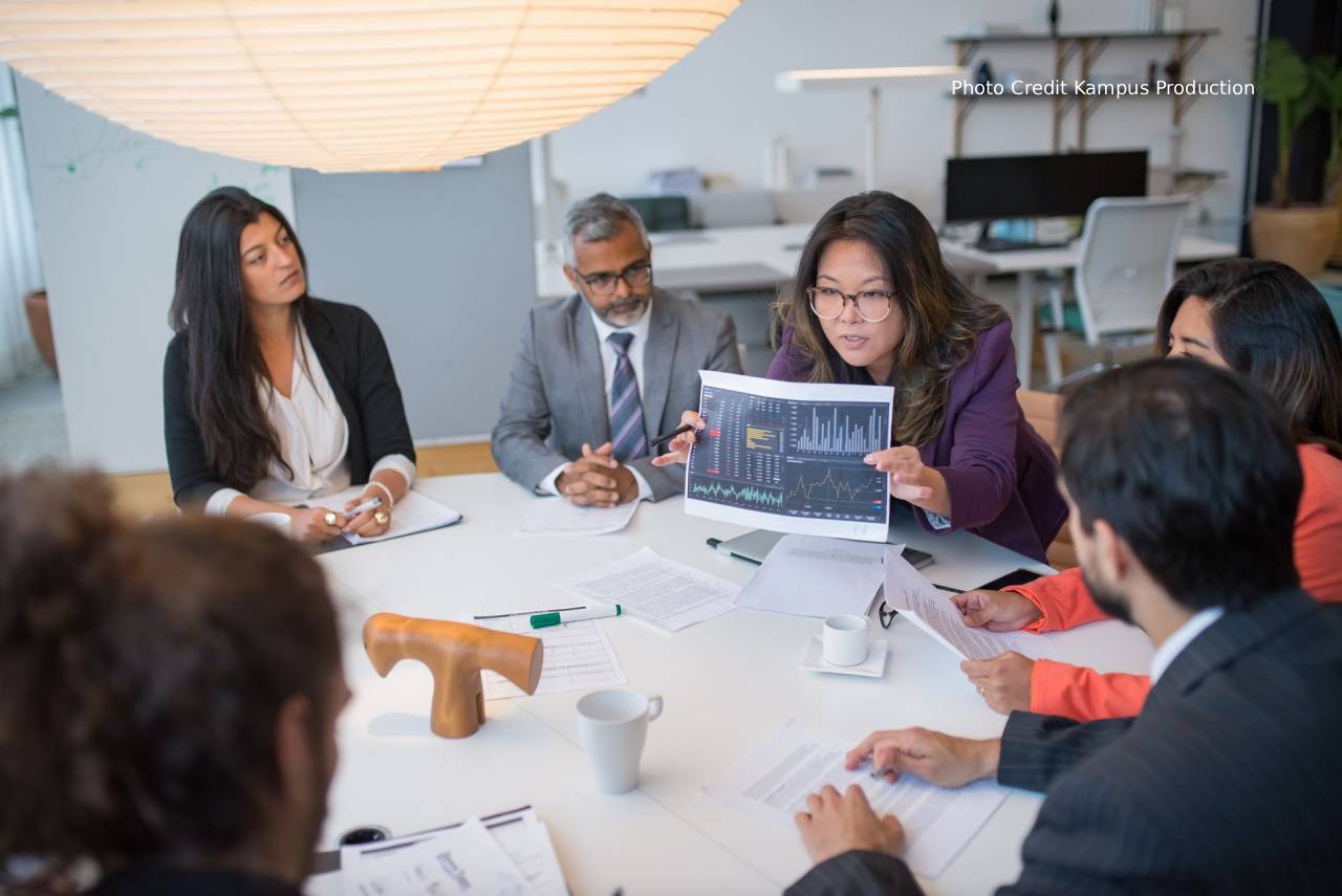 A boardroom table split between AI pilots still running in isolation and AI systems already integrated across functions, illustrating a governance screen for AI investment