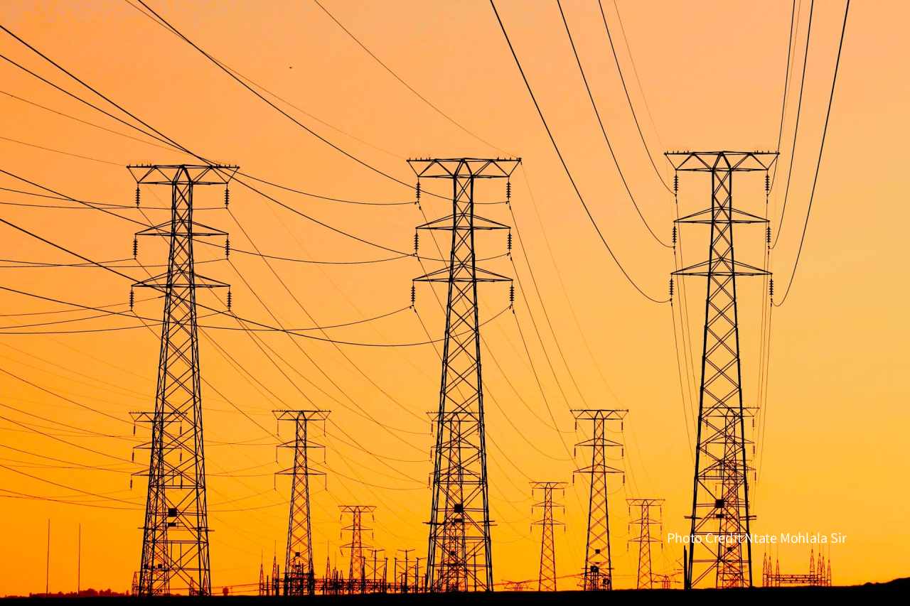 A checklist overlaid on a transmission tower and solar farm, representing the due-diligence variables that predict whether an energy project gets built